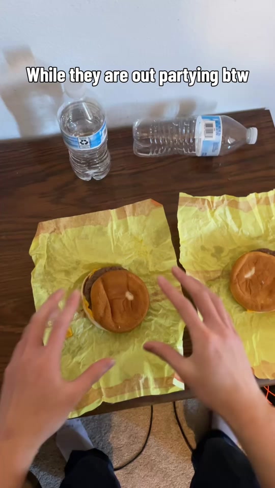 A frame of a trend example by @ryu_da_sigma on TikTok: hands wrapping burgers beneath the caption While they are out partying btw.